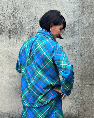 Person wearing a blue plaid dress standing against a concrete wall.