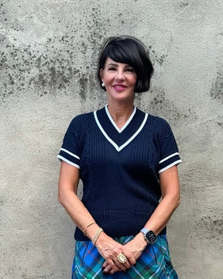 Woman in a blue and green plaid skirt standing against a concrete wall.
