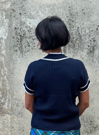 Person wearing a navy sweater and plaid skirt standing against a textured wall.