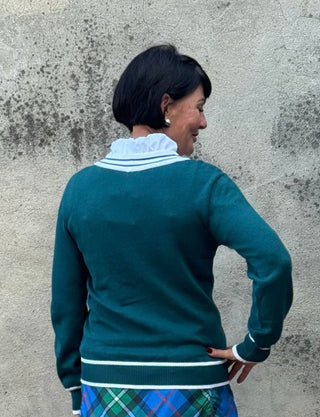 Person wearing a green sweater and plaid skirt against a textured wall.