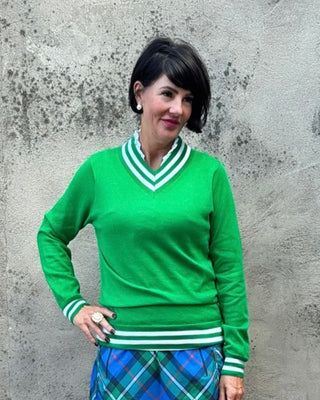 Person wearing a green sweater and plaid skirt standing against a textured wall.