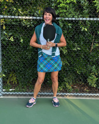 Woman holding a paddle on a pickleball court with greenery in the background