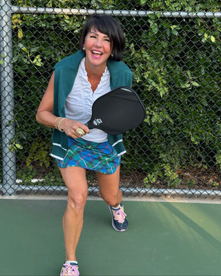 Woman holding a pickleball paddle on a tennis court with greenery in the background