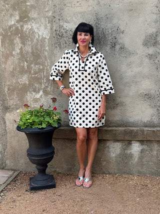 woman in a black and creme polka dot dress next to a urn with flowers