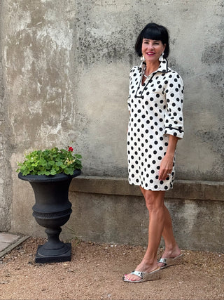woman in a black and creme polka dot dress next to a urn with flowers