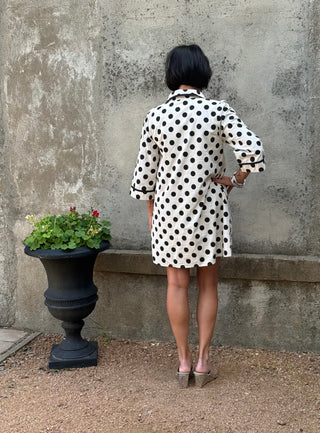 back view of a woman in a black and creme polka dot dress next to a urn with flowers