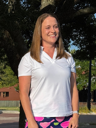 Woman wearing a white polo shirt and colorful pants standing outdoors with trees in the background