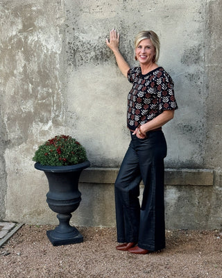Woman standing next to a stone wall with a decorative urn and plant