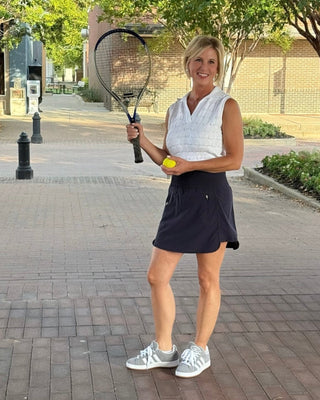 Woman holding a tennis racket and ball on a paved walkway with trees in the background