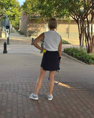 Person standing on a sidewalk holding a tennis racket and ball