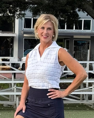 Woman posing outdoors in front of a building with trees and a white fence.