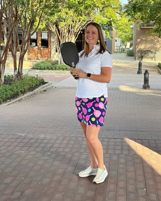 Woman holding a pickleball paddle on a sidewalk with trees and buildings in the background