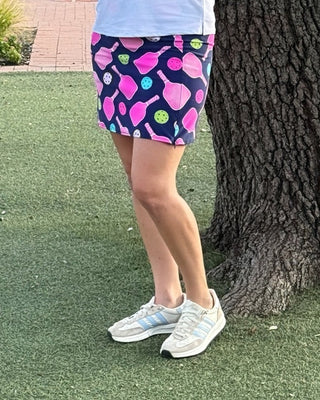 Woman holding a pickleball paddle standing next to a tree on a pickleball court.