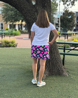 Person wearing a colorful skirt and white shirt standing in a park-like setting with a large tree.