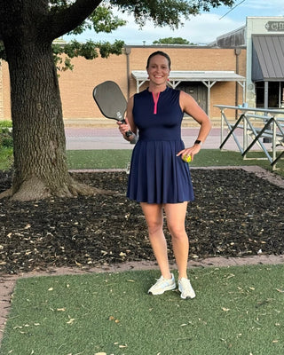 Woman in a navy dress holding a paddle on a grassy area with a building and tree in the background