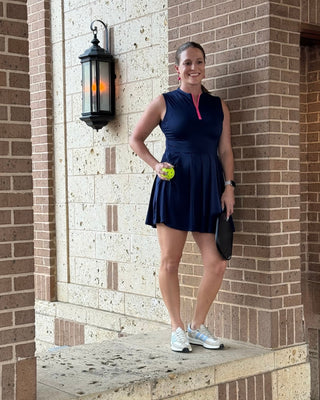 Woman in a navy blue dress standing against a brick wall