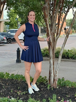 Woman in a blue dress standing outdoors near trees and a road.