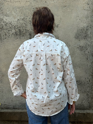 A person viewed from behind wearing a white long-sleeve button-up shirt with a small brown and gray dachshund print, paired with blue jeans, standing against a textured concrete wall.