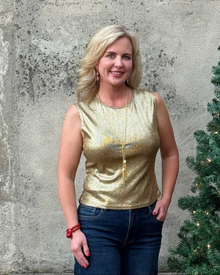 Woman in a gold top and blue jeans standing next to a decorated Christmas tree against a concrete wall.