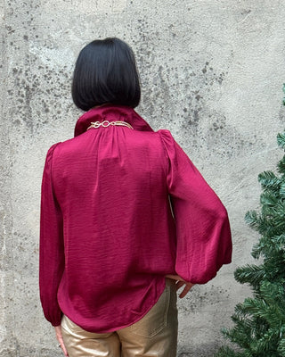 Person wearing a red hoodie and gold pants standing next to a Christmas tree on a concrete floor.