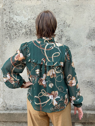 woman standing in front of a concrete wall in a green silky blouse and tan linen pants- back view