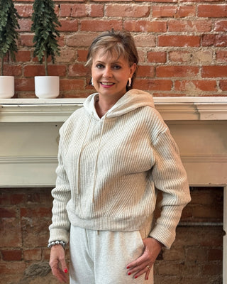 Woman in a cream-colored outfit standing in front of a brick wall with decorative elements.