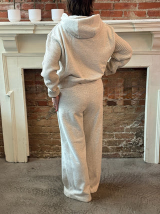 Person wearing a beige tracksuit standing in front of a fireplace.
