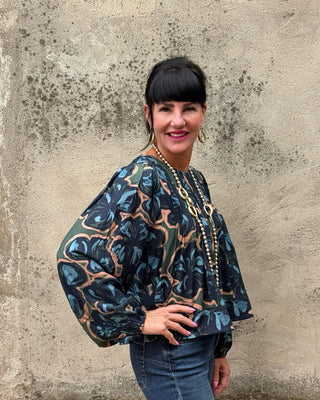 Navy abstract botanical print top by Fun 2 Fun with pintuck pleats, balloon sleeves, and banded hem styled with dark wash jeans and long gold necklace