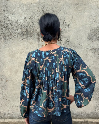 Navy abstract botanical print top by Fun 2 Fun with pintuck pleats, balloon sleeves, and banded hem styled with dark wash jeans and long gold necklace-back view
