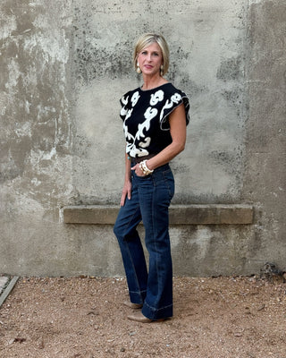 Blonde woman against a concrete wall in a western black and creme  print top and jeans