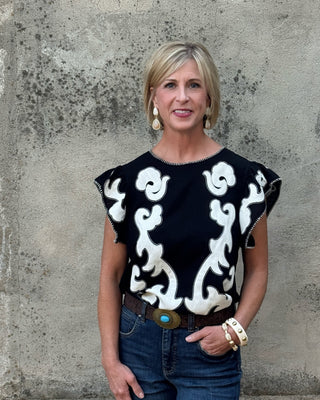 Blonde woman against a concrete wall in a wester black and creme  print top