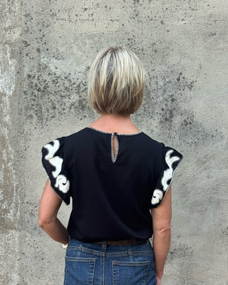 back view of Blonde woman against a concrete wall in a western black and creme  print top