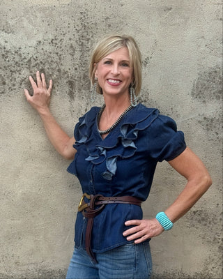 Blonde woman standing against a concrete wall in a ruffled denim top and jeans