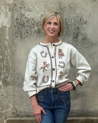 Western inspired cream cardigan with knit horses, horseshoes, zigzag pattern, and brown whipstitch trim on neckline and button placket
