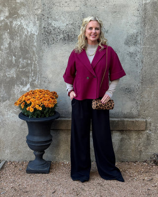 blonde woman standing in front of a conctrete wall with black pants and a maroon jacket