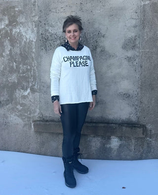 Person wearing a sweater with 'CHAMPAGNE PLEASE' text standing against a textured wall with snow on the ground.