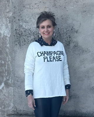 Person wearing a sweater with 'CHAMPAGNE PLEASE' text standing against a textured wall with snow on the ground.