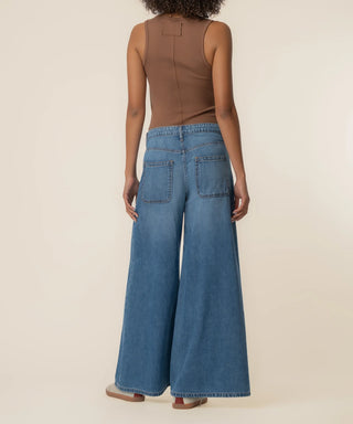 Person wearing a brown sleeveless top and blue wide-leg jeans on a beige background