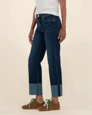 Person wearing a white t-shirt and dark blue jeans on a beige background