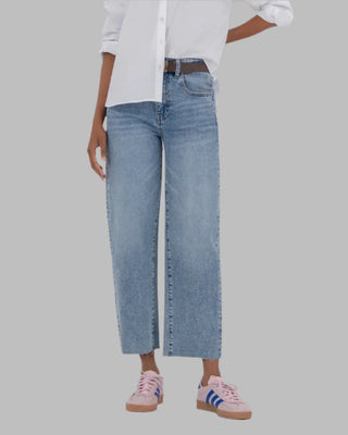 Person wearing a white button-up shirt, blue jeans, and sneakers on a beige background