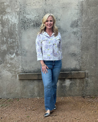 Woman wearing a lavender floral blouse  by Jodifl and Kut from the Kloth Kelsey jeans standing against a concrete wall.
