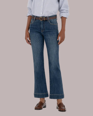 Person wearing a light blue checkered shirt, dark blue jeans, and brown shoes on a beige background