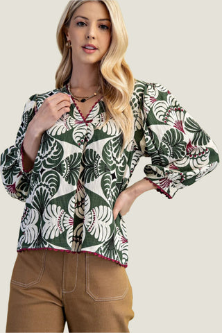 Woman wearing a patterned blouse with long sleeves against a light green background
