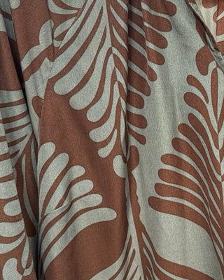 A brown and sage green patterned blouse hanging on a wooden hanger on a clothing rack, with other garments visible in the background.
