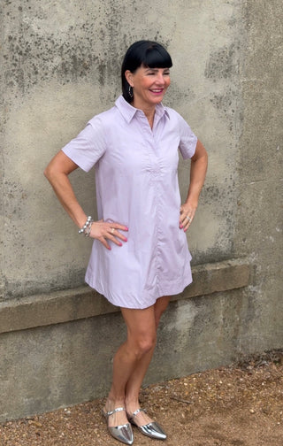 Woman wearing a light purple dress standing against a textured wall.