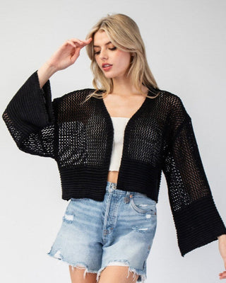 Woman wearing a black knit cardigan and denim shorts on a white background
