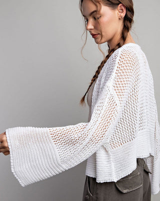 Woman wearing a white knit top with bell sleeves against a gray background