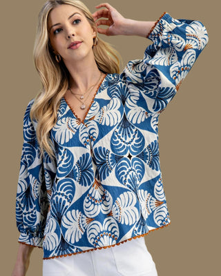 Woman wearing a blue and white patterned blouse with white pants on a green background