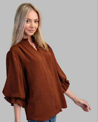 Woman wearing a brown blouse and blue jeans against a green background