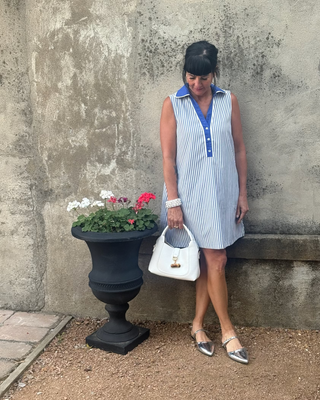 Woman in a bue & white striped dress against a wall next to flowers